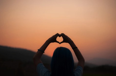 Persona haciendo forma de corazón al atardecer